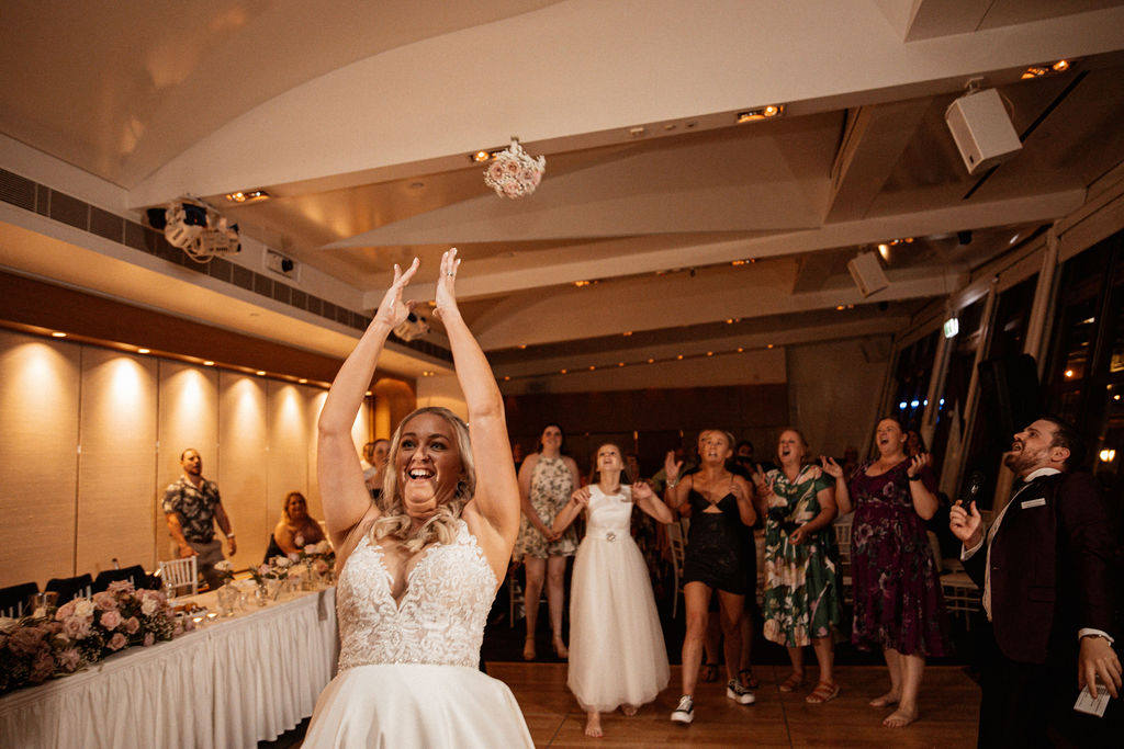 A bride throwing a bouquet backwards towards a group of women